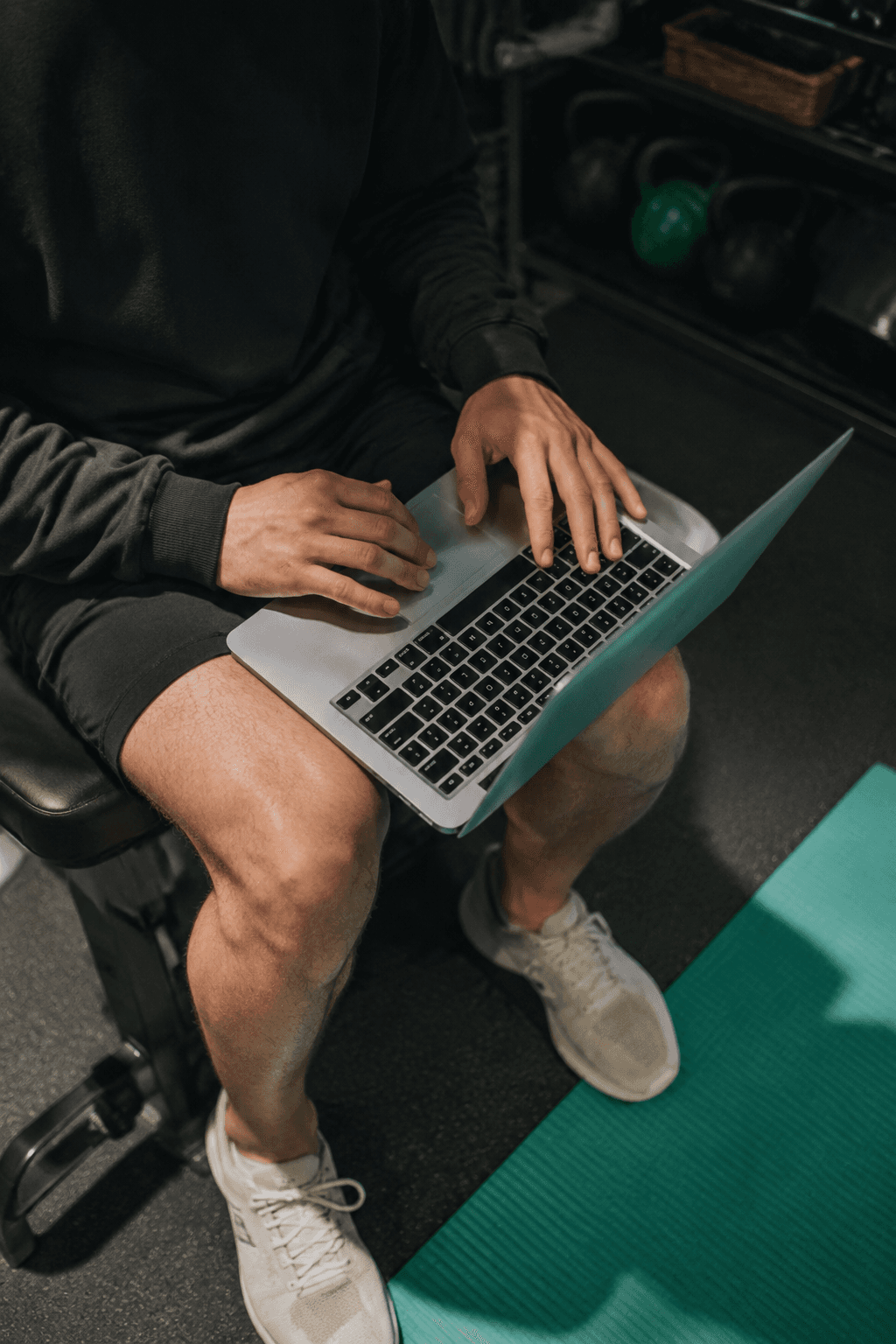 Close-up of a trainer using a laptop in the gym beside an exercise mat.